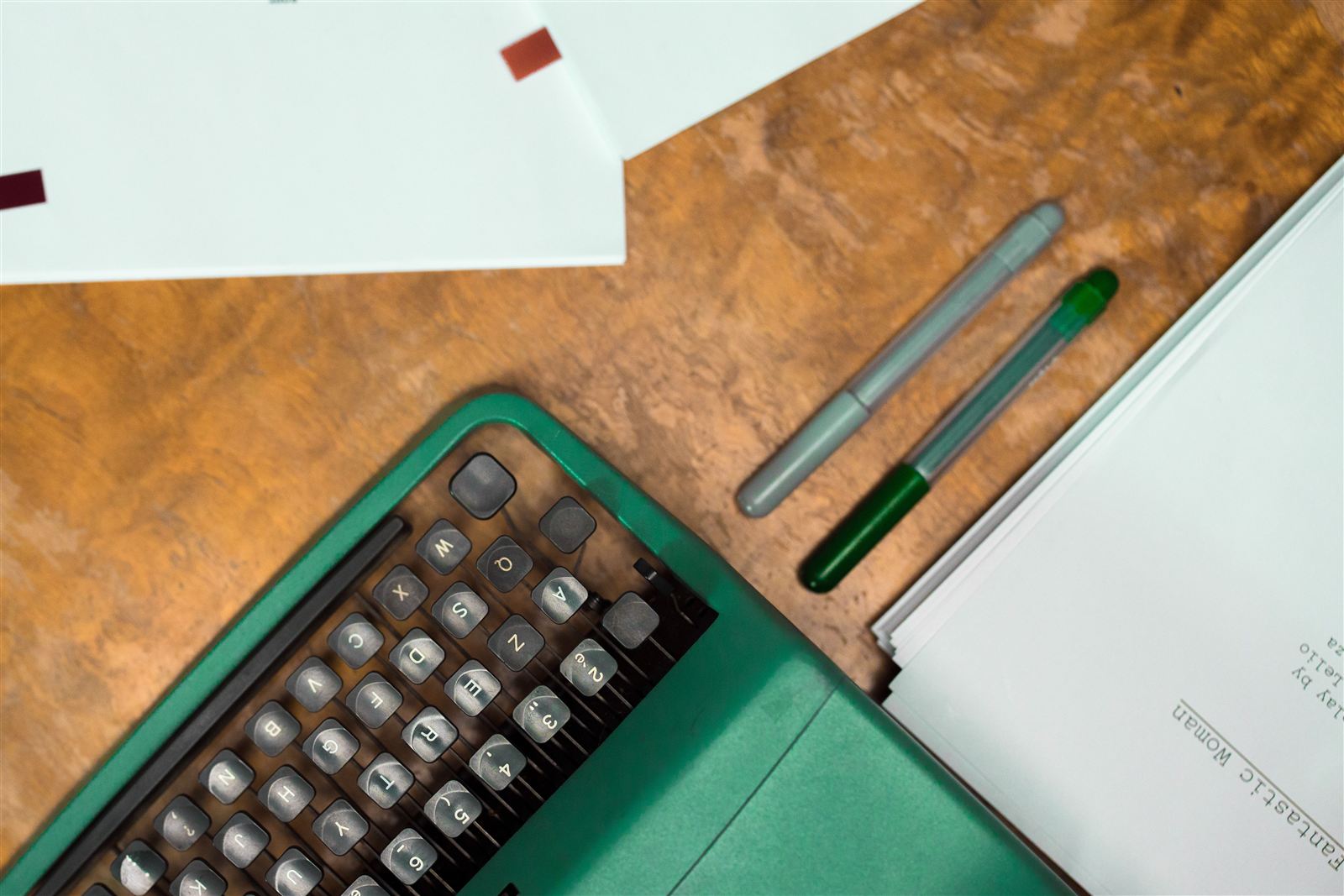 Une machine à écrire, des stylos et des pages de manuscrit imprimées sur un bureau en bois, prêtes pour une relecture