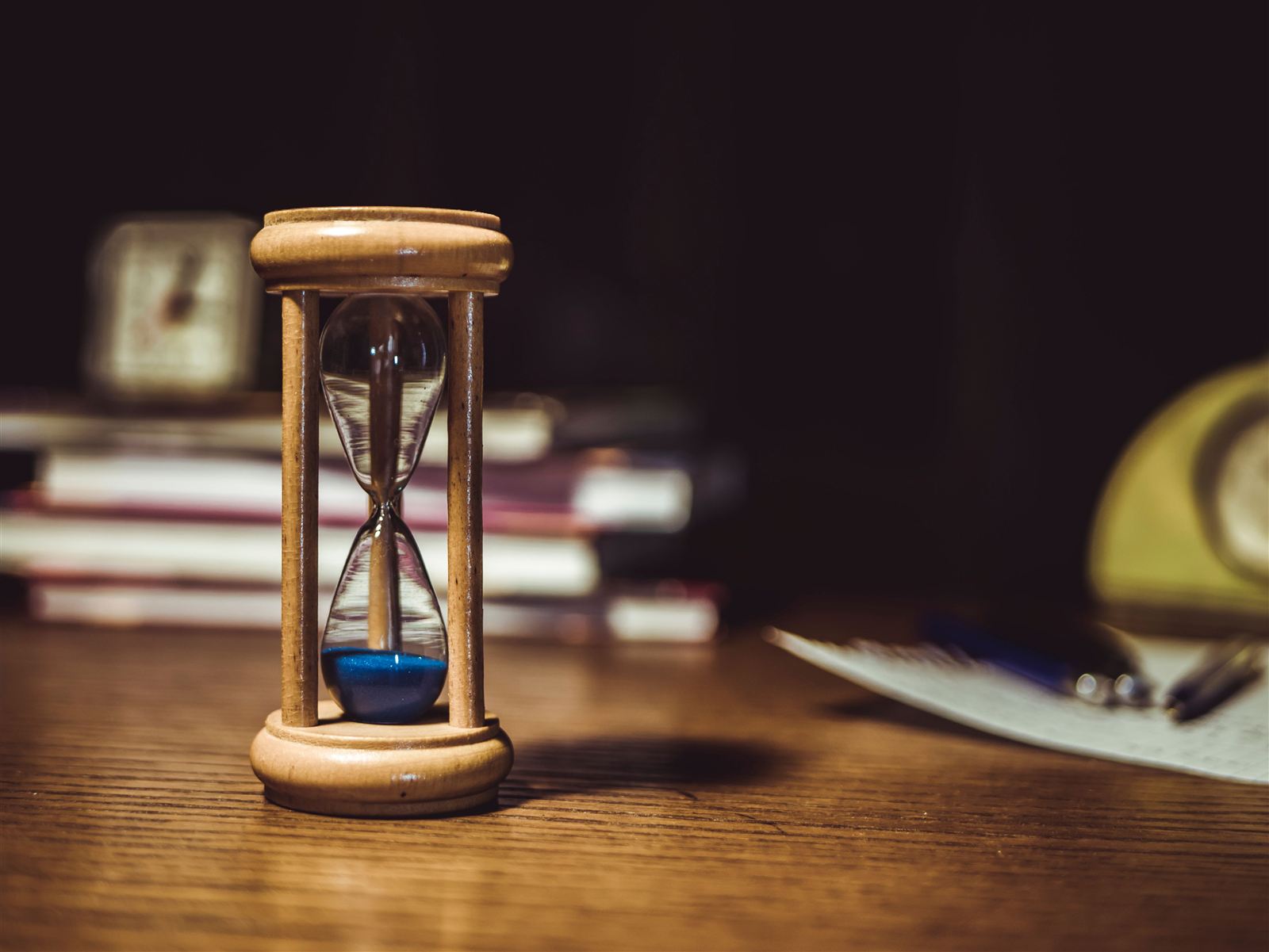 Un sablier au sable bleu posé sur un bureau en bois, entouré de livres et d'un carnet, symbole du temps chronométré d'un sprint d'écriture